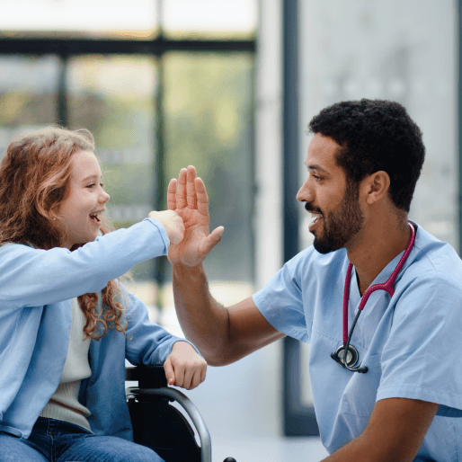 A male doctor high-fives a  smiling young girl patient in a wheelchair.