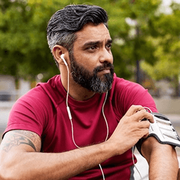 A middle-aged man with a dark beard is deep in thought listening to ear-pods