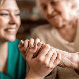 In a close-up of their clasped hands, a smiling granddaughter holds her grandmother’s hand affectionately