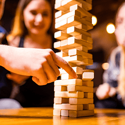 A close up image of the game Jenga and a family gathered around playing
