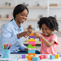 A smiling child mental health professional builds a tower of colorful blocks with a happy five-year-old girl
