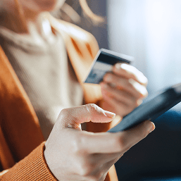 A close-up image of a woman holding her phone with her right hand and her credit card in her left
