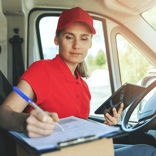 A woman wearing a red cap and uniform sits behind the wheel of a vehicle, writing up paperwork