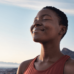 A close-up of a young woman smiling with her eyes closed by the sea