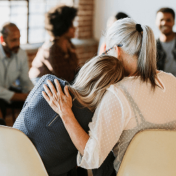 In a photo from behind, a woman receives a hug from another woman at a support group meeting